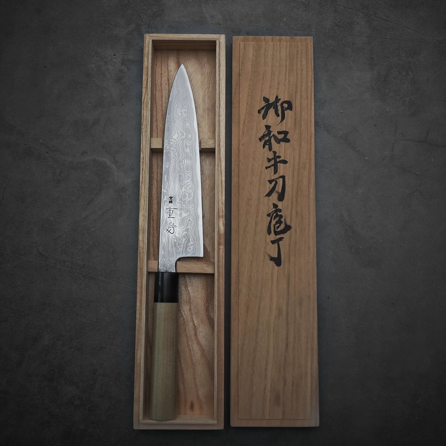 Kitaeji Japanese chef's knife in a wooden box with engraved text on a dark background