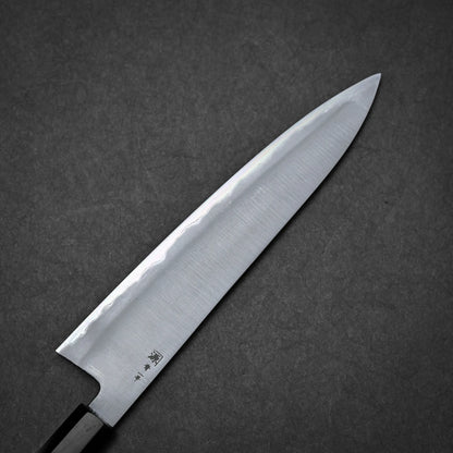 A close-up of a kasumi Japanese chef's knife with a sharp, pointed blade and a dark handle, set against a dark gray textured background.