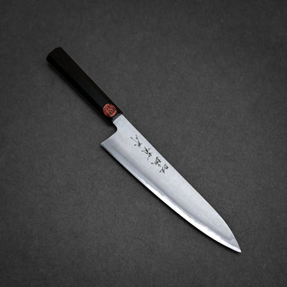 A kasumi chef's knife with a dark handle and a steel blade featuring engraved Japanese characters, shown on a dark gray textured surface.