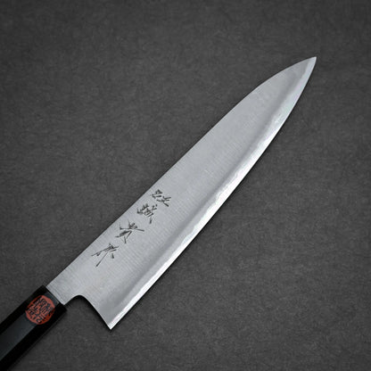A kasumi gyuto Japanese-style kitchen knife with a sharp, pointed blade and kanji characters engraved on it, photographed on a dark gray textured surface.