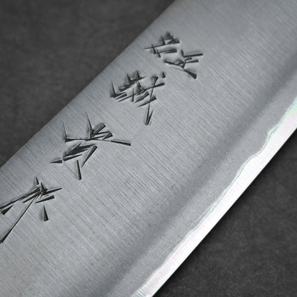 Close-up of a kasumi gyuto blade with Japanese characters engraved near the edge, highlighting the fine texture and sharpness of this workhorse gyuto against a dark background.