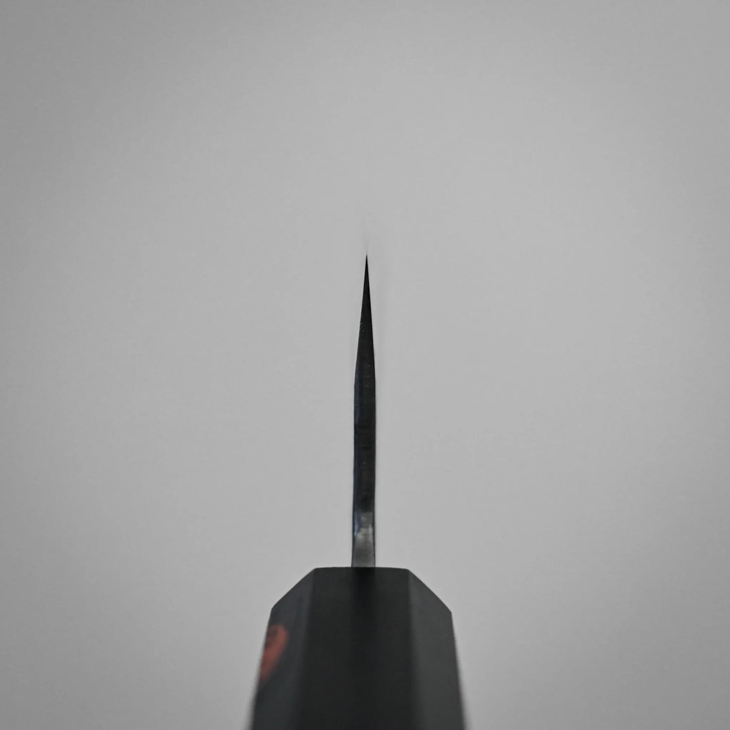 Choil shot of a workhorse gyuto blade, centered against a plain, light gray background. The knife's handle is partially visible at the bottom of the image.