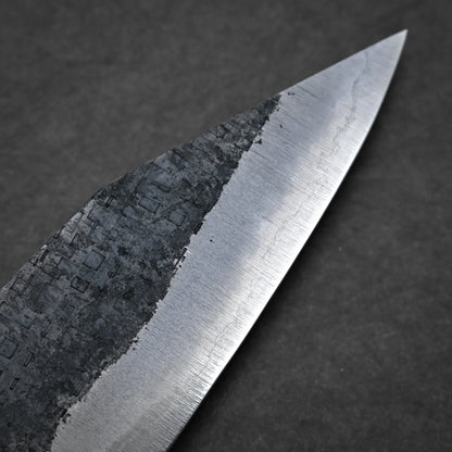 Close-up view of a workhorse gyuto blade, featuring a textured, dark upper section and a smooth, polished lower edge against a plain dark background.