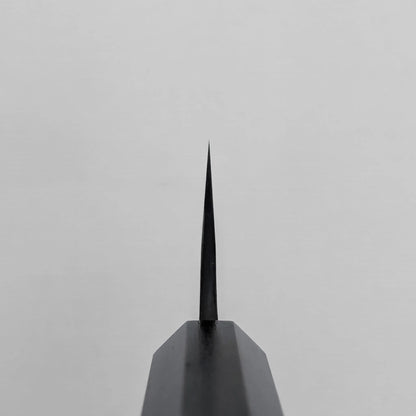 Choil shot of a knife blade positioned vertically against a plain light gray background, highlighting the thinness and edge.