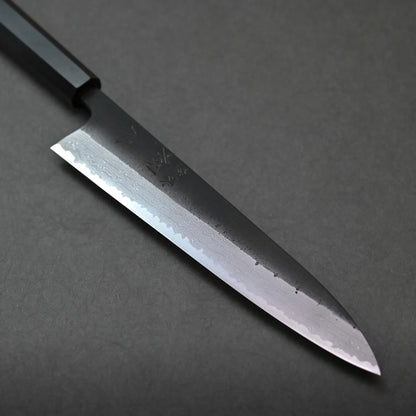 A close-up view of a Japanese chef’s knife with a patterned blade and black handle, set on a dark, textured surface.