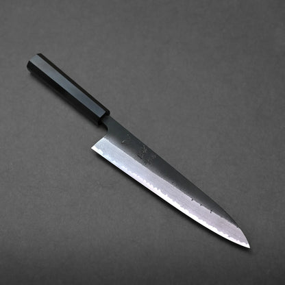 A Japanese-style chef's knife with a pointed blade and a black angular handle rests on a dark, textured surface.