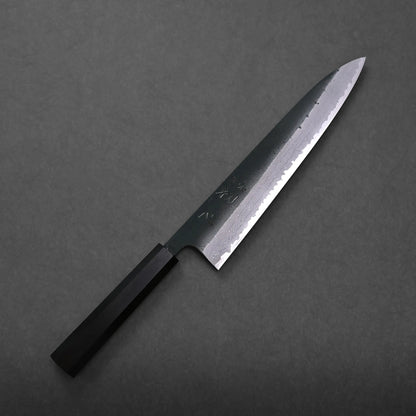 Hatsukokoro Shinkiro kurouchi damascus AS gyuto 240mm chef’s knife with a dark, straight handle and a beautifully patterned blade rests on a dark, textured surface.