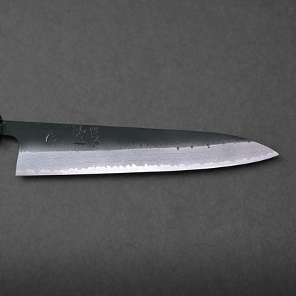 A Japanese chef’s knife with a pointed blade showcasing a visible Damascus pattern and engraved characters, photographed against a plain dark background.