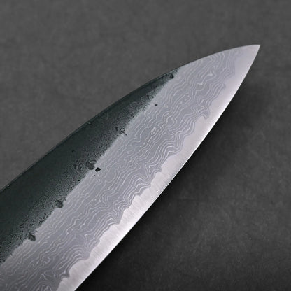 Close-up of a knife blade featuring a distinct wavy Damascus steel pattern, set against a dark background. The blade displays an intricate design and water droplets near the spine.
