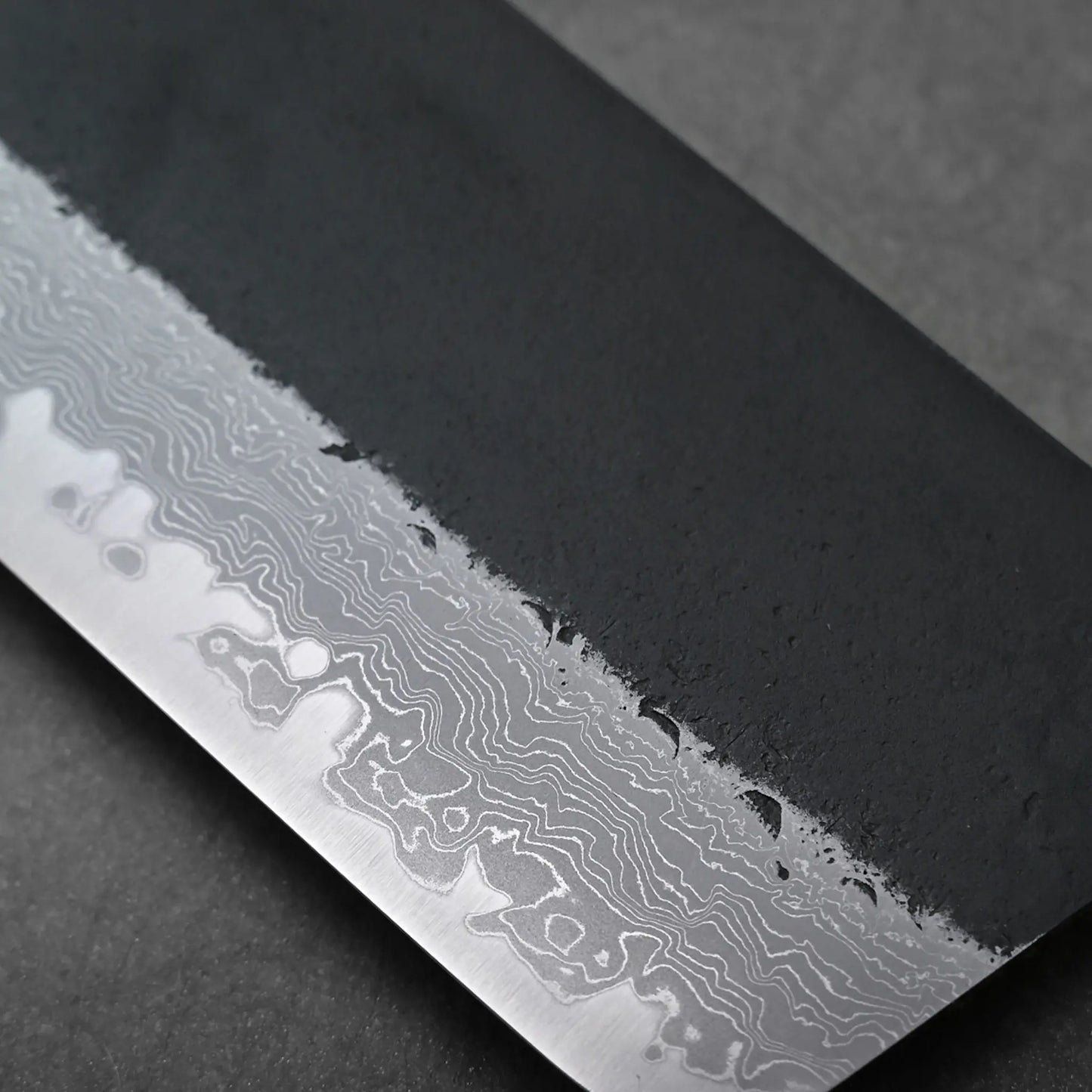 Close-up of a Japanese knife blade showing wavy Damascus patterns; the blade shape is not fully visible in this view.