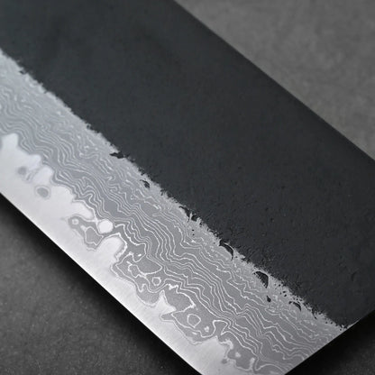 Close-up of a Japanese knife blade showing wavy Damascus patterns; the blade shape is not fully visible in this view.