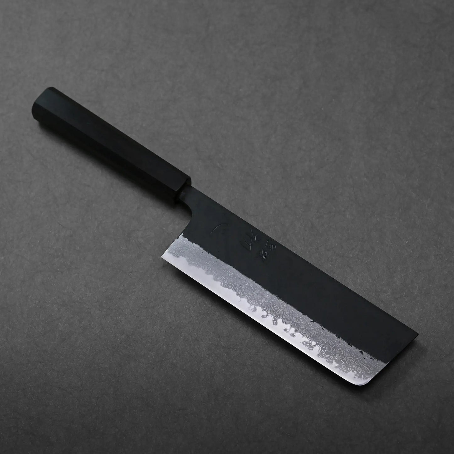 A rectangular-bladed Japanese knife, likely a nakiri, features a dark handle and hand-forged finish.