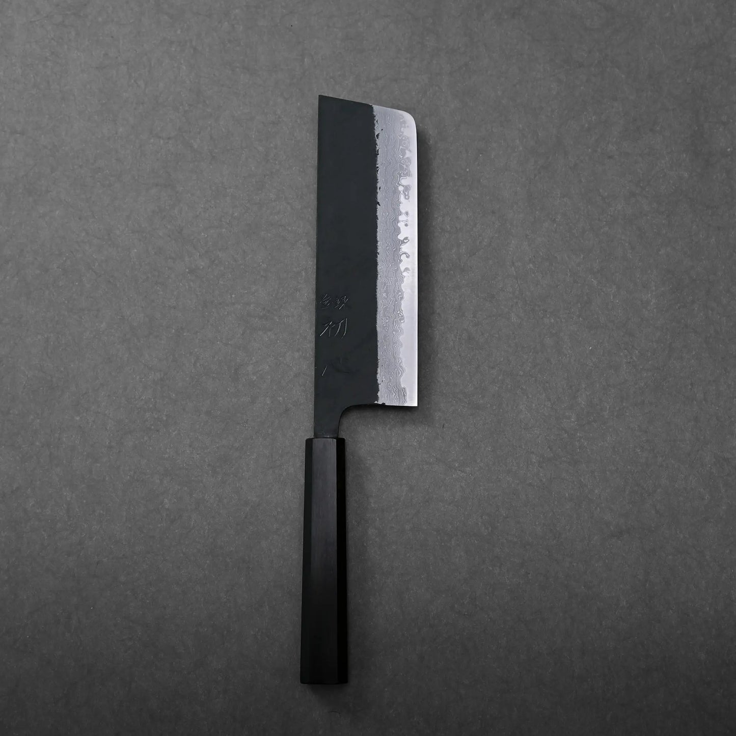 The image shows a dark-handled Japanese knife with a straight-edged blade, resembling a nakiri, blade finish unclear.
