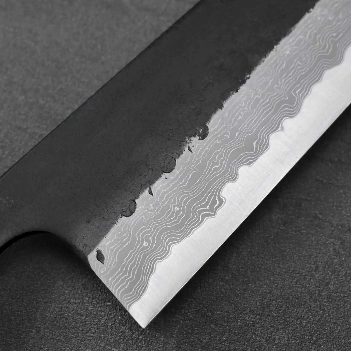 Gyuto blade close-up featuring damascus steel with a distinct wavy pattern on the surface.
