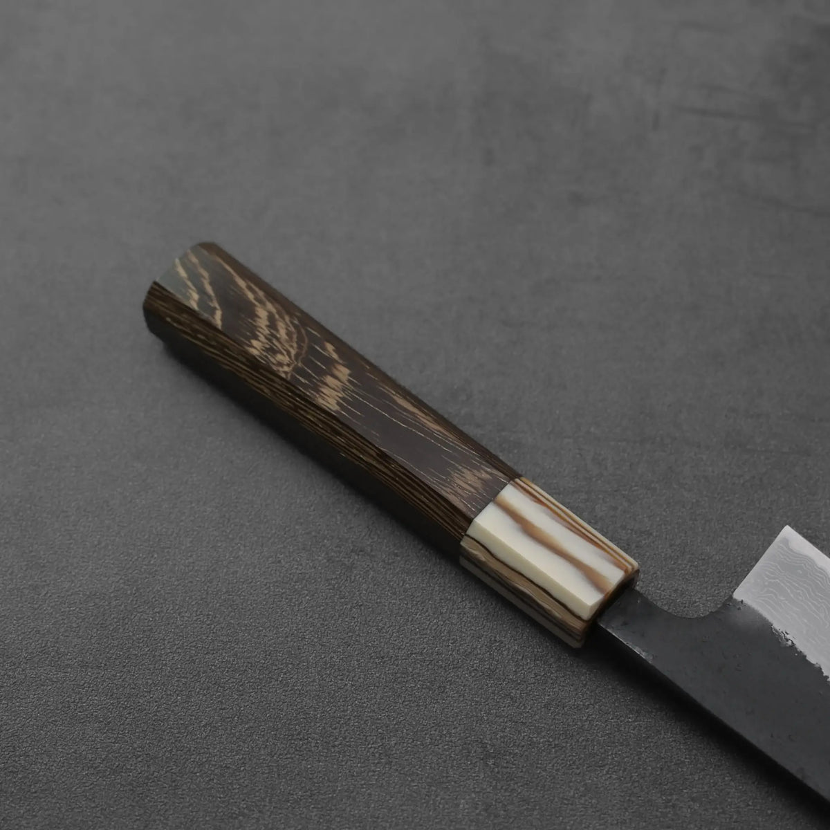 A close-up of a gyuto, highlighting its damascus pattern and kurouchi finish.