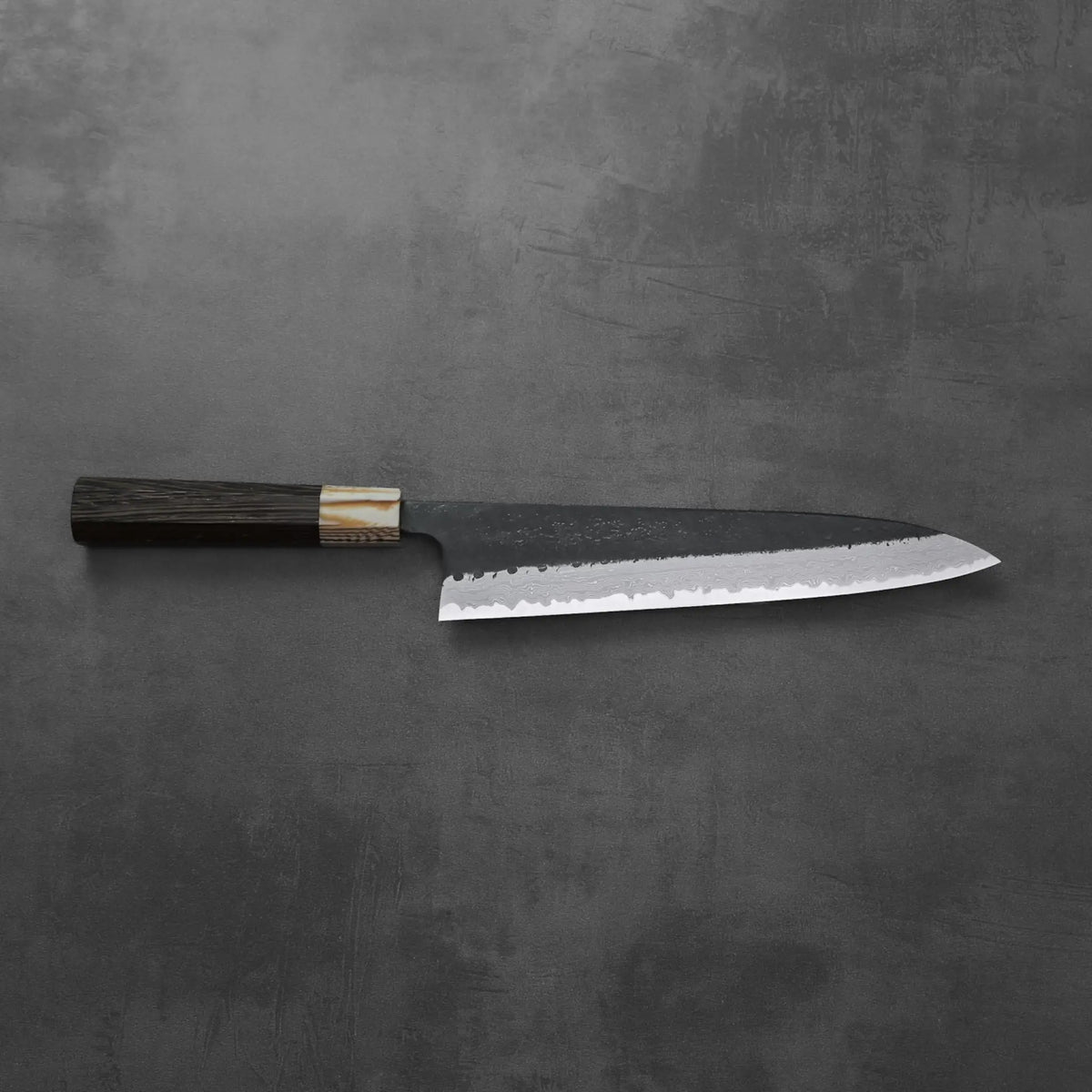 Gyuto with a dark handle, damascus pattern visible along the blade. No other objects are present.