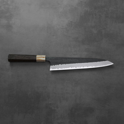 Gyuto with a dark handle, damascus pattern visible along the blade. No other objects are present.
