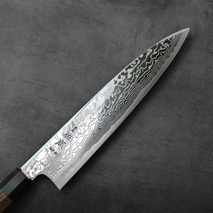 A close-up of a gyuto blade, showing layered Damascus steel pattern and fine detailing on the knife.