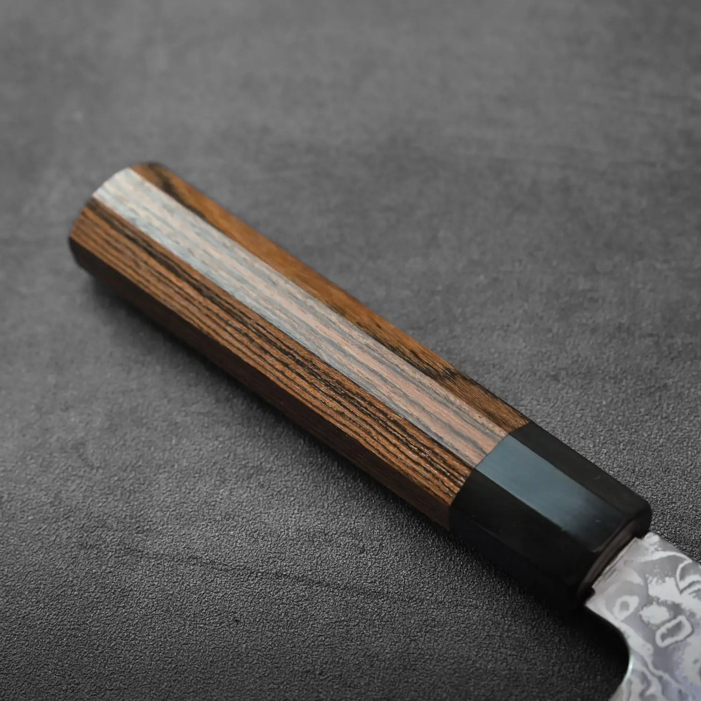 Gyuto knife handle close-up with a dark bolster, highlighting texture and detailing on the grip area.