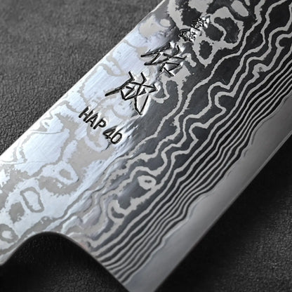 Gyuto blade in close-up, featuring damascus steel with intricate etched patterns and Japanese characters.