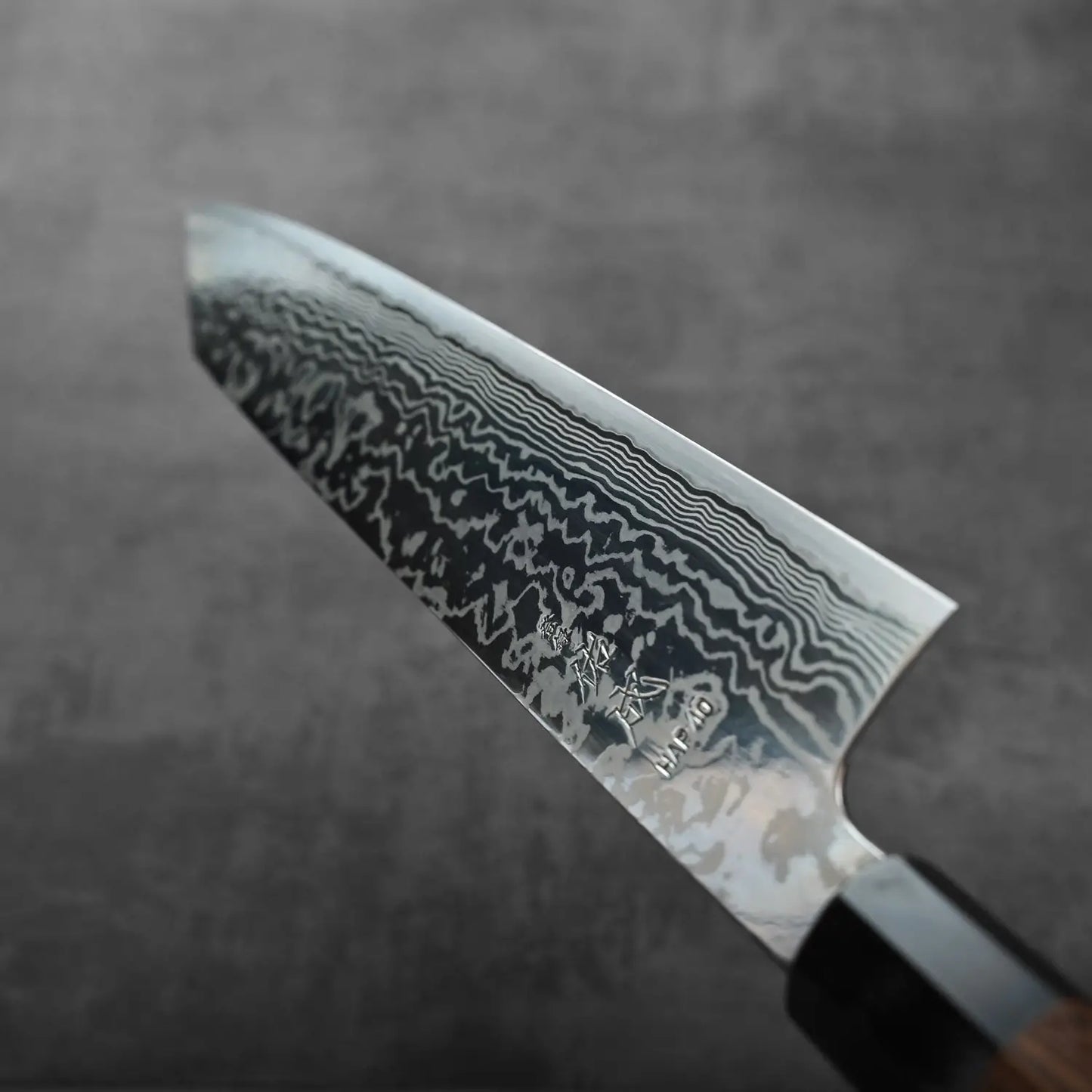 A close-up of a kiritsuke gyuto featuring a patterned blade with intricate damascus detailing.