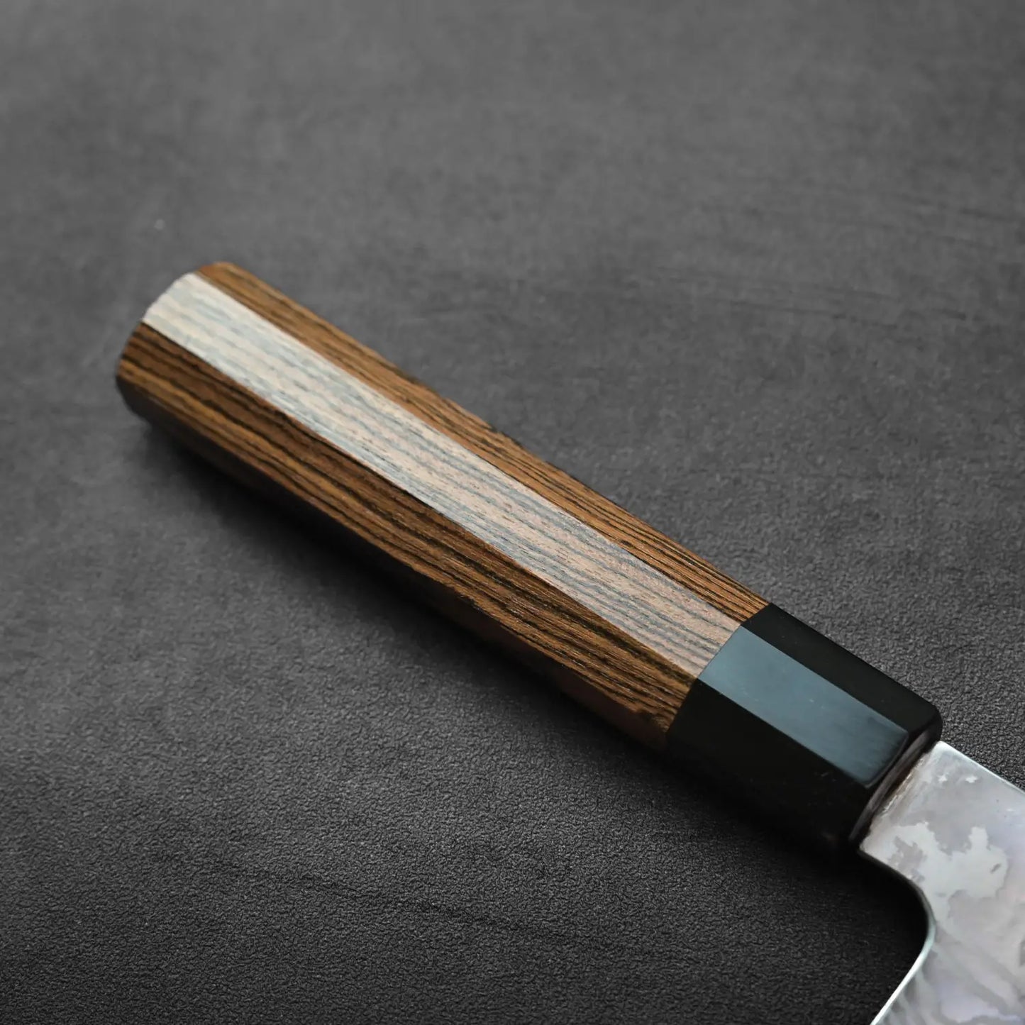 Close-up of kiritsuke gyuto handle with black bolster, detailed damascus pattern visible on the metal.