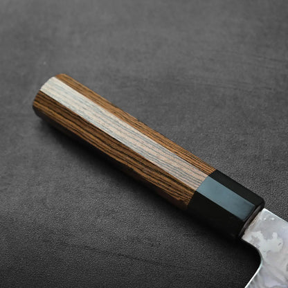 Close-up of kiritsuke gyuto handle with black bolster, detailed damascus pattern visible on the metal.