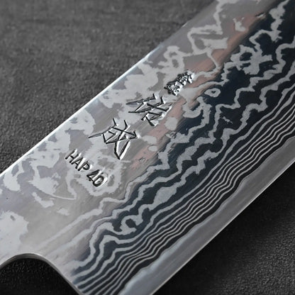 Close-up of a kiritsuke gyuto blade, showing damascus patterns and engraved text along the 270mm steel.