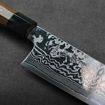 Kiritsuke gyuto blade showing a wavy Damascus pattern and engraved details in a close-up view.