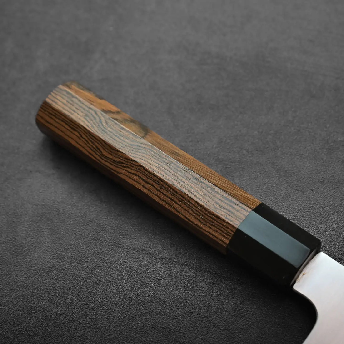 Close-up of a gyuto's wooden handle with dark bolster, highlighting its shape and wood grain details.