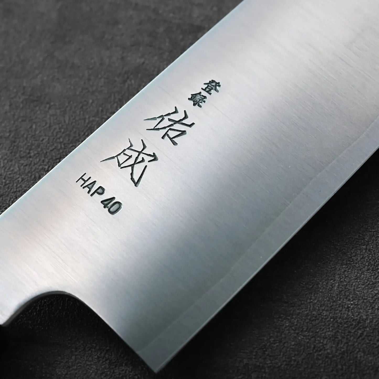 Close-up of a gyuto blade, showcasing Japanese characters engraved on the metal surface of the knife.