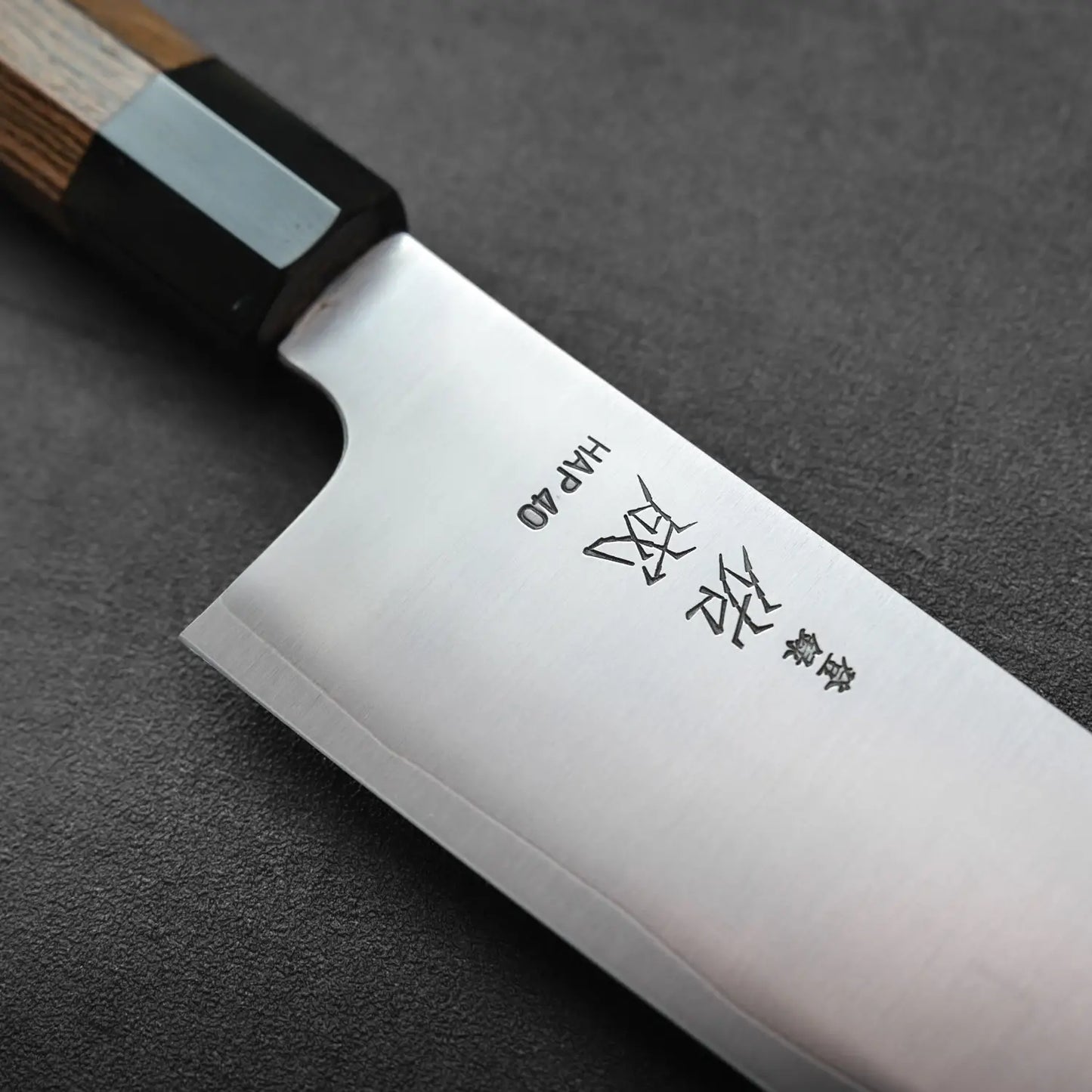 Close-up of a gyuto with engraved characters on the blade, focusing on details and metallic texture.