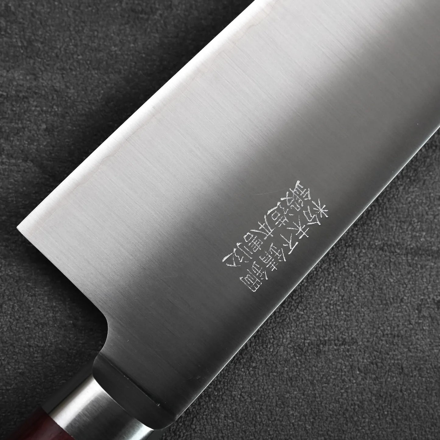Close-up of a gyuto blade with engravings in focus, showing metal texture and detailed markings.
