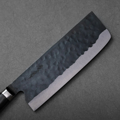 A close-up of a nakiri with a hammered black blade, showing intricate texture and details of the knife.