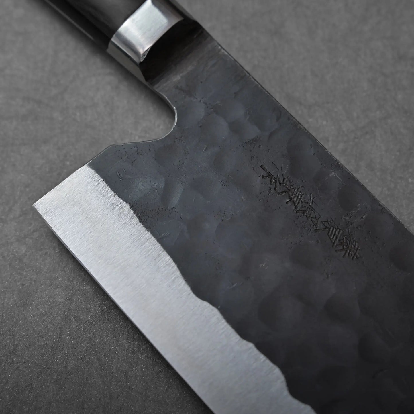 Nakiri with a hand-forged black finish and hammered texture, shown in a close-up.