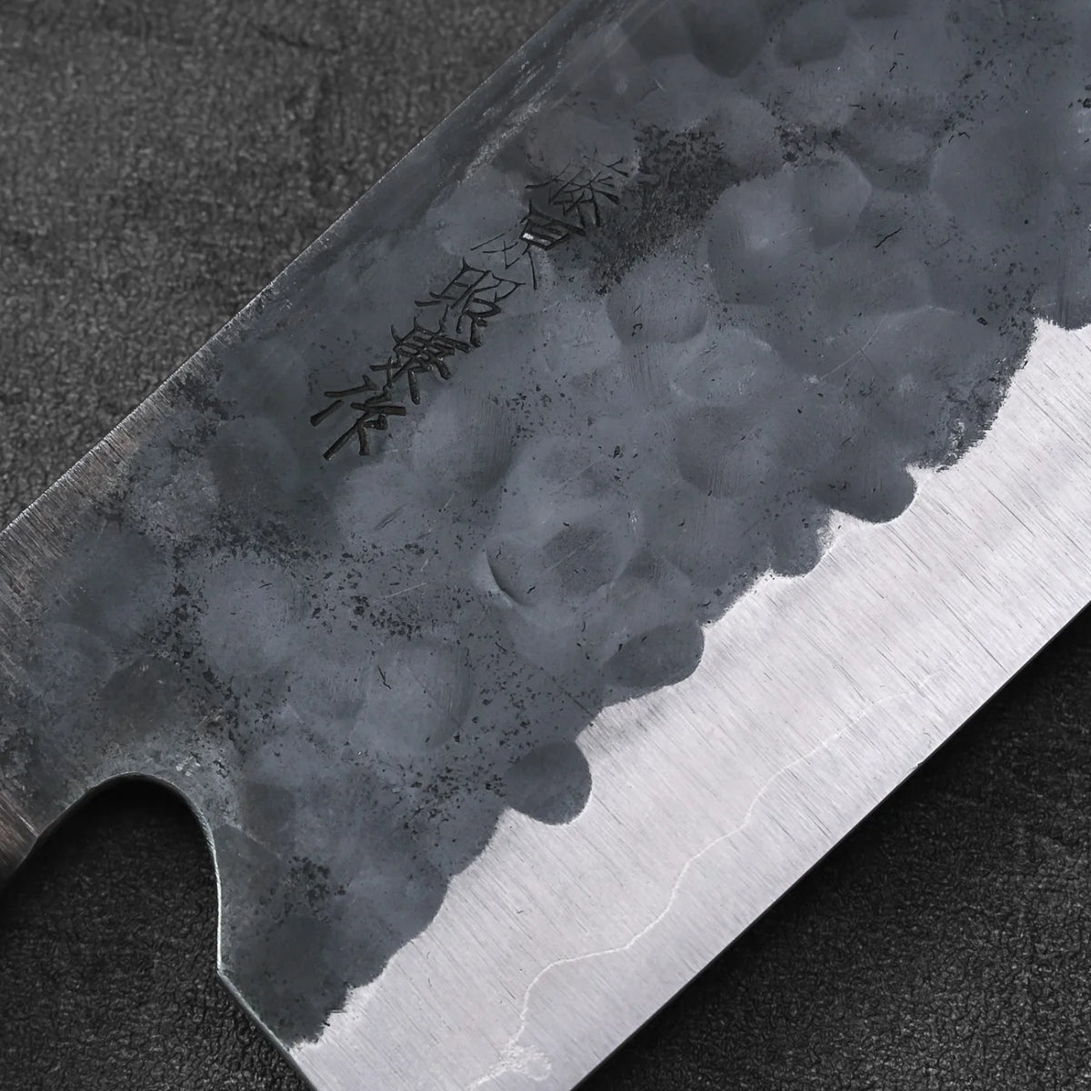 Close-up of a bunka blade with engraved text, featuring a tall profile and visible texture.