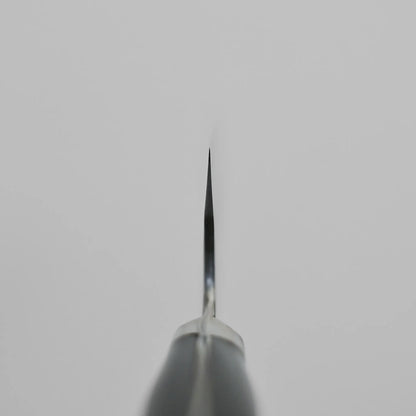 Close-up of a Teruyasu Fujiwara Maboroshi shirogami#1 gyuto 240mm blade, photographed from the tip with the edge facing the camera, set against a plain light gray background.