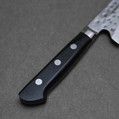 Close-up of a hand-forged Teruyasu Fujiwara Maboroshi shirogami#1 gyuto 240mm handle with three metal rivets, attached to a dark material and resting on a gray surface; part of the blade appears at the top right corner.