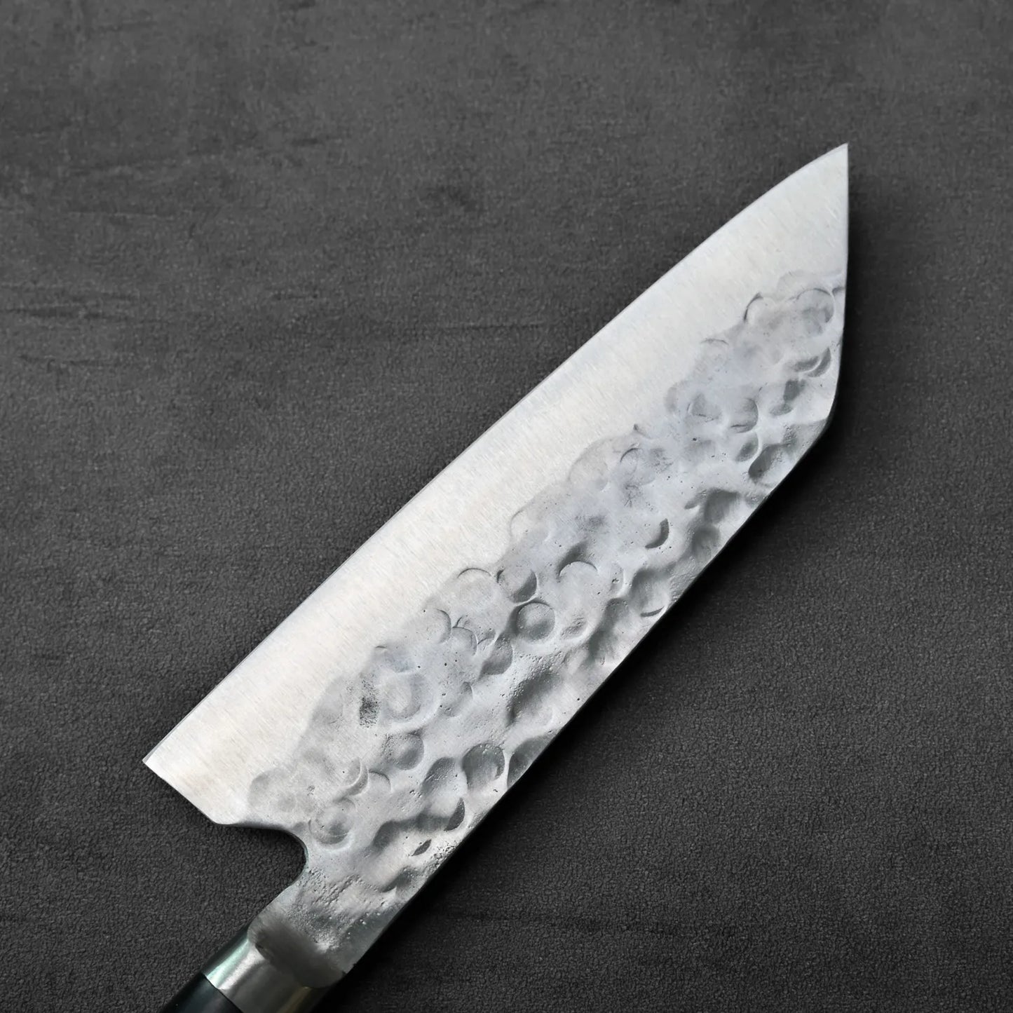 Close-up of a santoku with a hammered blade, highlighting metal texture and distinctive patterning.
