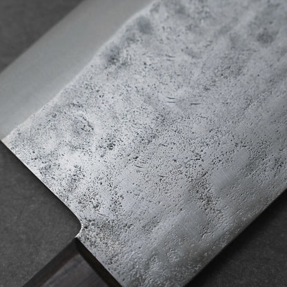 Close-up of the Teruyasu Fujiwara nashiji shirogami#1 chuka bocho 210x90mm blade, showcasing its mottled nashiji finish with fine scratches and patterns; the knife handle appears partially in the lower left corner.