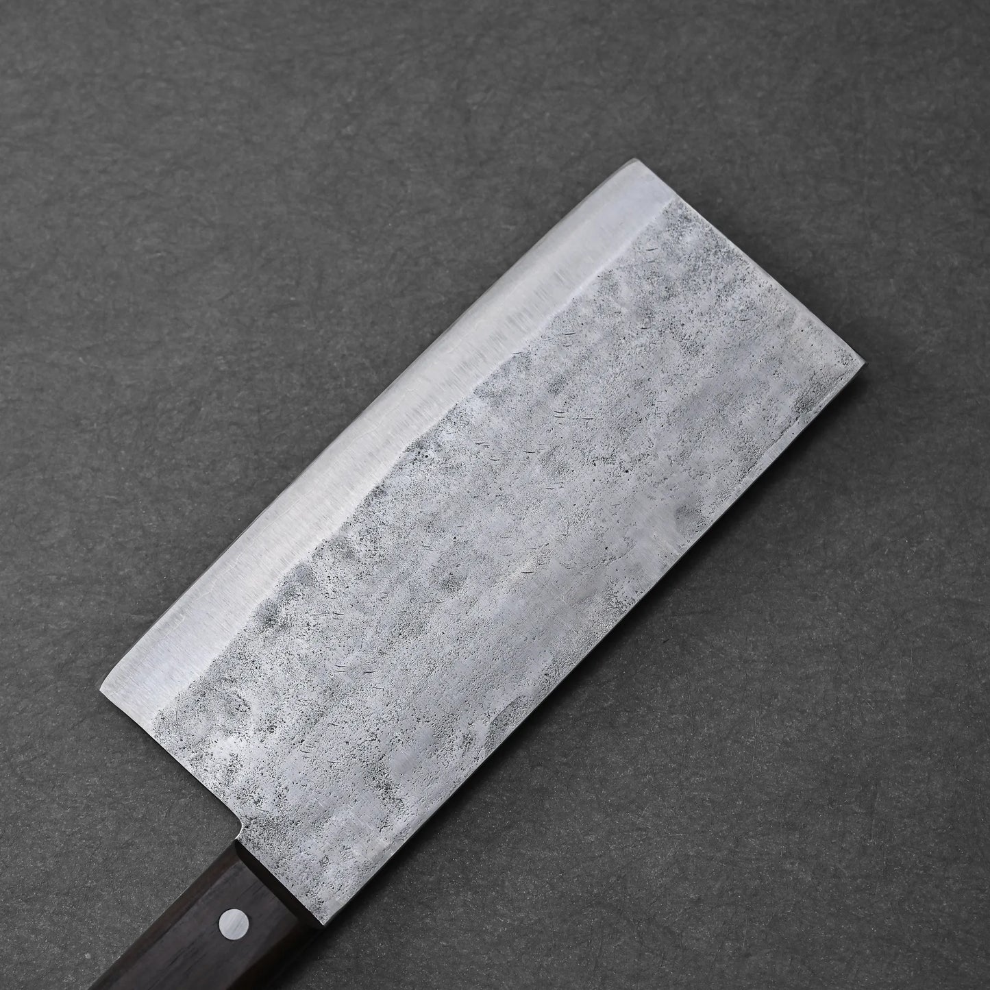 A close-up of the Teruyasu Fujiwara nashiji shirogami#1 chuka bocho 210x90mm, a rectangular silver knife with a dark wooden handle, resting on a dark gray textured surface.