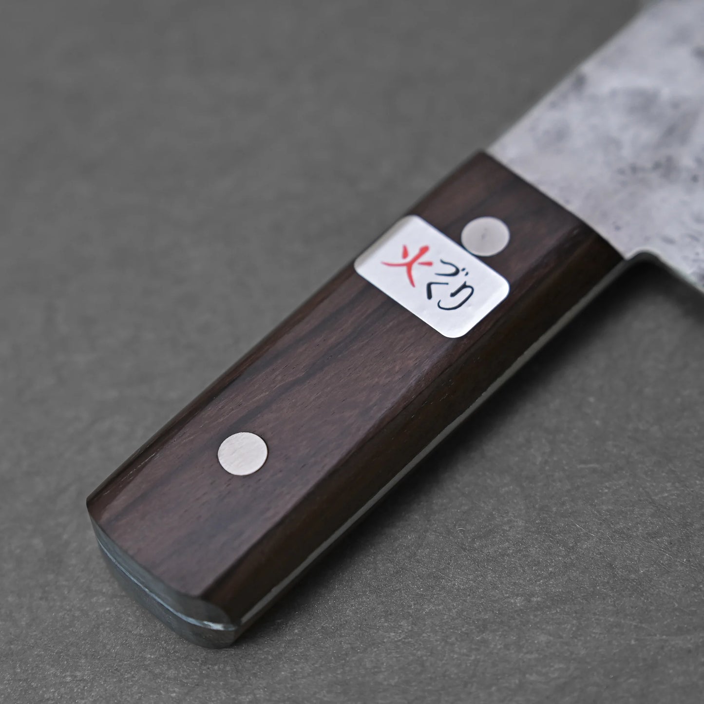 Close-up of the Teruyasu Fujiwara nashiji shirogami#1 chuka bocho 210x90mm, showing its dark wooden handle with two metal rivets, a rectangular label with Japanese characters (one in red), and a partially visible Shirogami#1 steel blade.