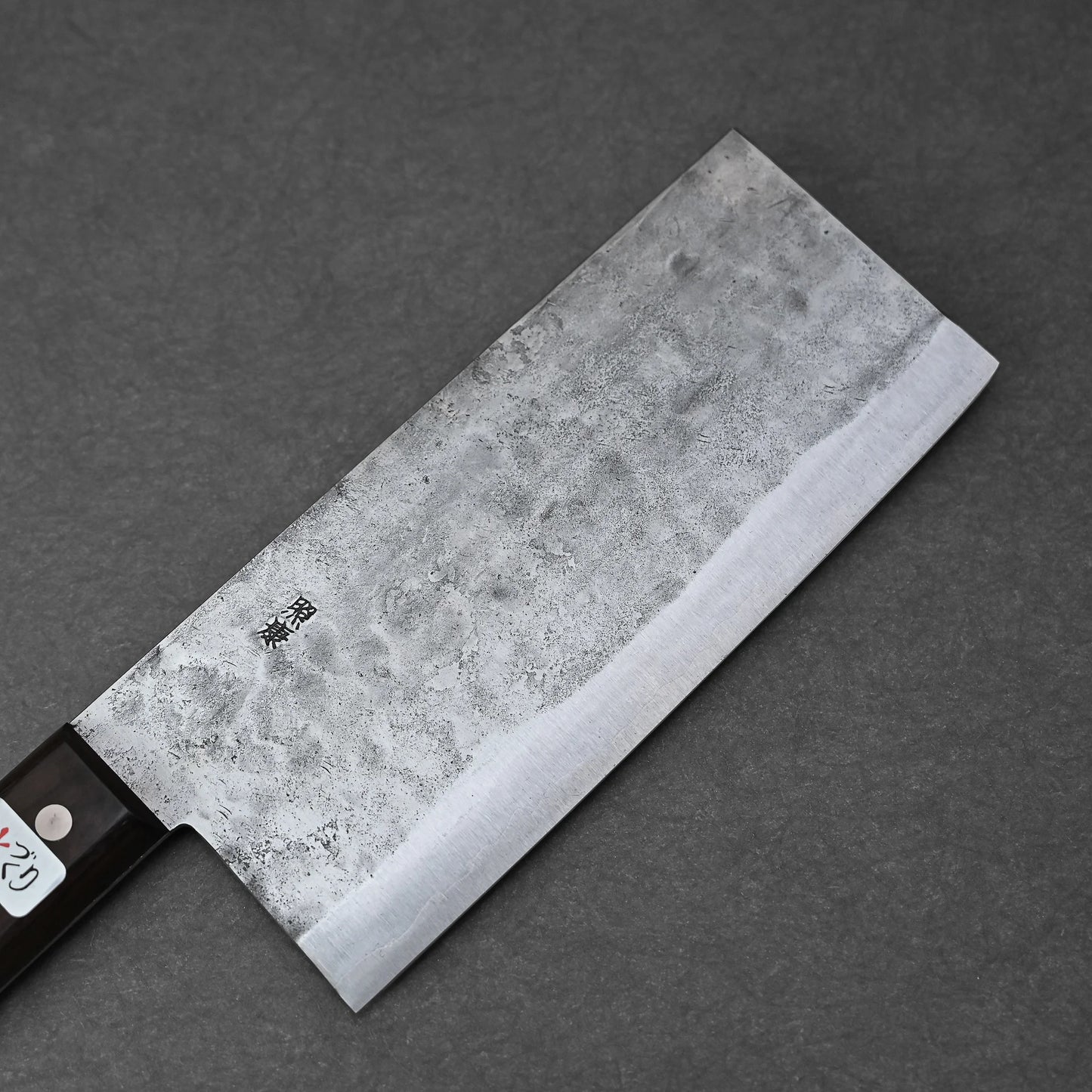 The Teruyasu Fujiwara nashiji shirogami#1 chuka bocho 210x90mm, featuring a rectangular hammered carbon steel blade and dark handle with a silver rivet, rests on a dark gray surface.