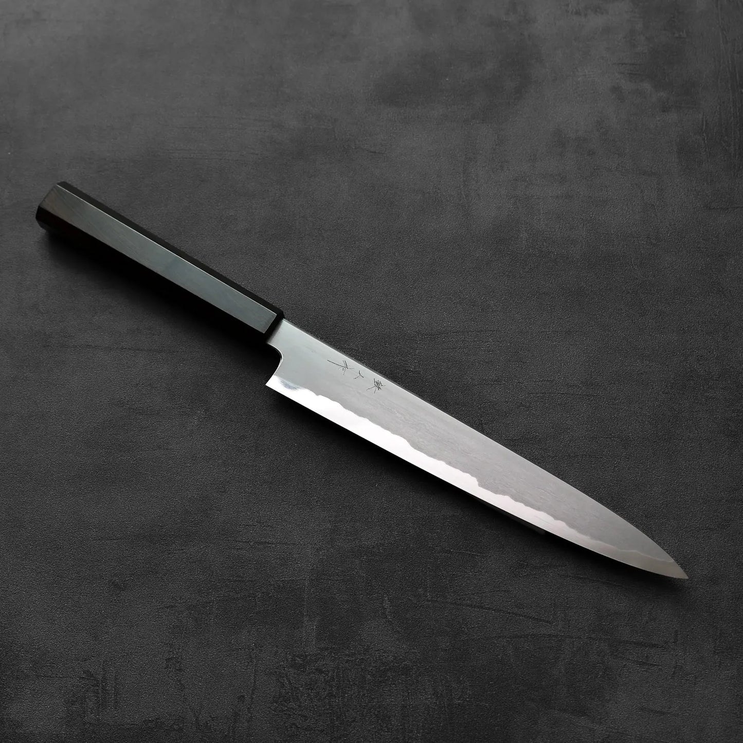 Sujihiki with a black handle is shown, highlighting the handle shape and details against a dark background.