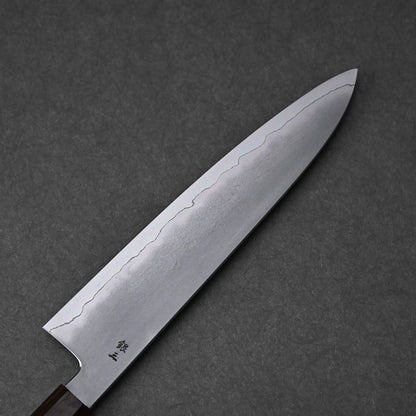 A full view of the reverse side of a gyuto knife blade. The ginsan stainless steel blade features a kasumi finish with a clear, wavy border extending along its length and tapering to a pointed tip. Kanji engravings are visible near the heel of the blade.