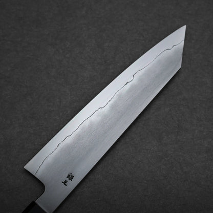 A close-up of a kiritsuke gyuto blade with a visible wavy hamon line and small black kanji characters near the handle, set against a dark textured background.