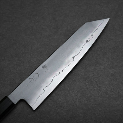A close-up of a kiritsuke Japanese chef knife with a straight edge and pointed tip, showing a visible wavy line pattern on the blade and Japanese characters etched near the handle, placed on a dark textured surface.