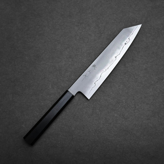 A Tetsujin kasumi ginsan kiritsuke gyuto 210mm with a black handle and a sharp, silver blade featuring subtle decorative patterns, placed on a dark gray textured surface.