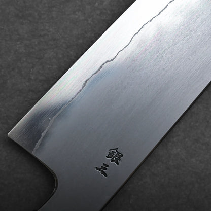 Close-up of a kiritsuke Japanese chef knife blade with a visible hamon line and Japanese characters engraved near the edge, set against a dark textured background.