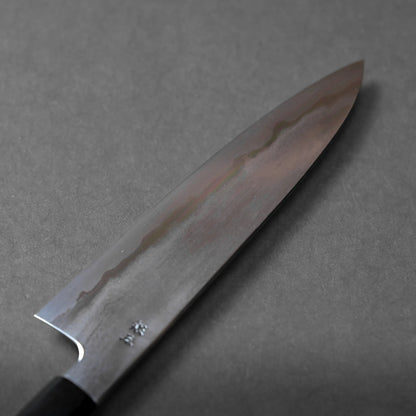 A close-up of a Japanese kitchen knife with a dark handle and a polished blade featuring a visible hamon pattern, displayed on a gray surface.